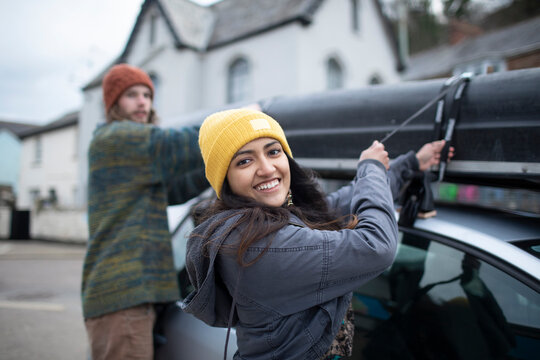Portrait happy young couple fastening canoe to top of car