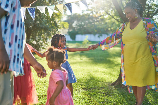 Happy grandmother and granddaughter dancing in sunny summer backyard