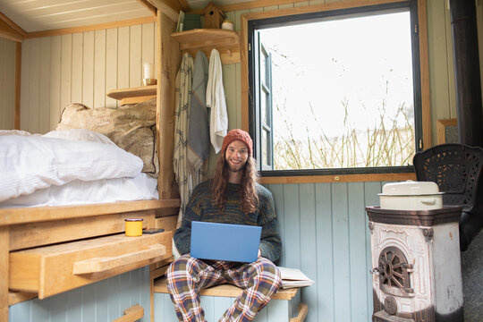 Portrait smiling young man using laptop in tiny cabin rental