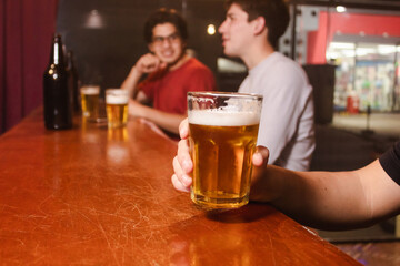 Detail shot of a man holding a glass of beer with his friends at the bar.