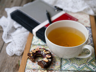 Green tea in big white cup with chocolate cookie on colored tray on a wooden background. Workpiece with notepad and pen. Planning. Breakfast. Close up.