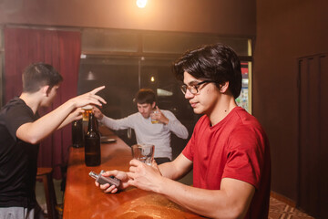 A young man drinking a beer while his drunken friends dance at the bar.
