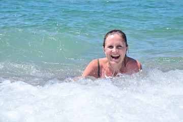 An adult attractive woman is swimming in the sea surf, she laughs with pleasure