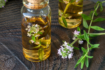 Thyme essential oil in a glass bottle and sprig of flowering thyme on a dark wooden background. Aroma oil preparation. Alternative medicine concept