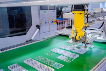 Pick and place yellow robotic arm manipulator moving flat plastic details on conveyor belt at modern robot trade show, exhibition. Manufacturing, engineering, industrial, automated technology concept