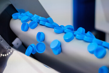 Many blue plastic bottle caps falling from conveyor belt at factory, exhibition - production line....