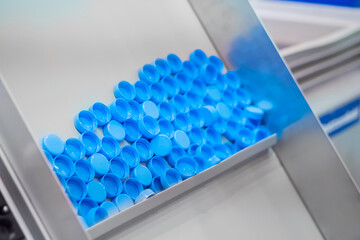 Many blue plastic bottle caps moving on conveyor belt of automatic compression molding machine at factory, exhibition: production line. Manufacturing, recycling, industry, technology equipment concept