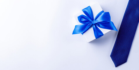 Fathers gift. White box with bow ribbon, blue bowtie or tie on light background. Concept of Fathers Day greeting card, copy space for text.