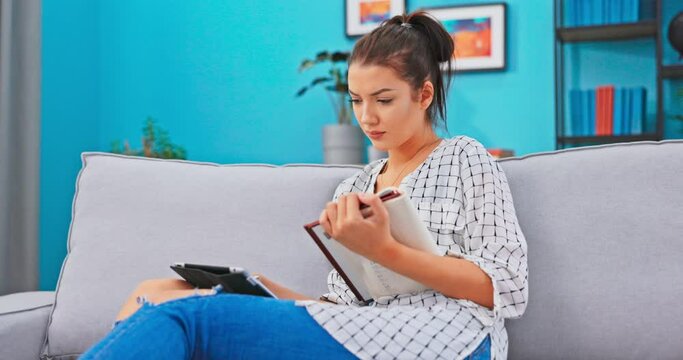 Busy woman, spends time studying with tablet and book, reads textbook, checks solved tasks, finds wrong answers is puzzled, grimaces on face, expresses incomprehension, contradicts head, gestures