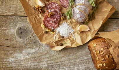 Italian salami wih sea salt, rosemary, garlic and nuts on paper. Rustic style. Close up.