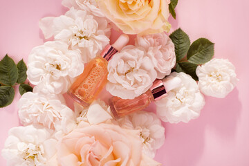 Essential rose oil in cosmetic bottle near fresh rose flowers against pink background.