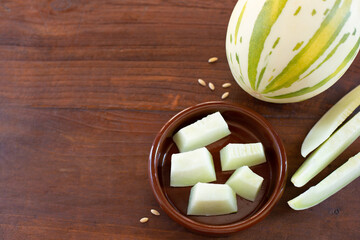 Ripe melon with green stripes and pieces of melon are on on a ceramic plate  on the background of a wooden table.. View from the top point. Copy space.
