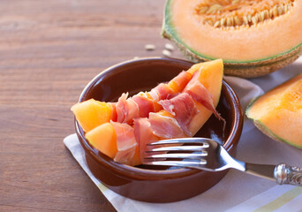 A round dish on which slices of fresh cantaloupe melon with jamon lie are on the background of a...