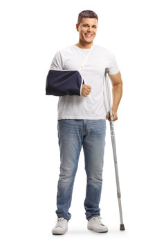 Full length portrait of a young man with a broken arm wearing an arm splint and standing with a crutch