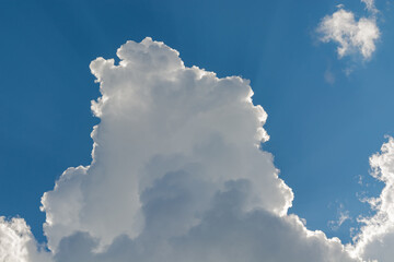 White fluffy clouds on the background of blue sky. The illumination of the Sun emphasizes their...