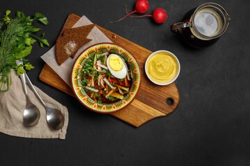 Cold soup .Okroshka, a traditional summer Russian dish.On a wooden board with croutons and mustard in a pot. On a black background, a copy of the space, overhead