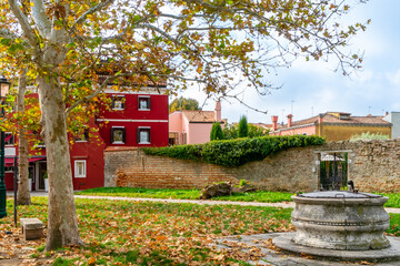 Small public square with fallen leaves from trees during autumn. In the background, some colored houses. Burano, Italy