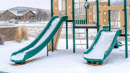 Pano Green slides of playground on snow covered neighborhood park against cloudy sky