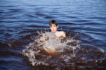 Boy swimming and splashing in the blue water of river, sea or lake