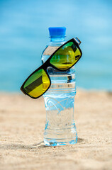 A bottle of drinking water and sunglasses on the sea beach