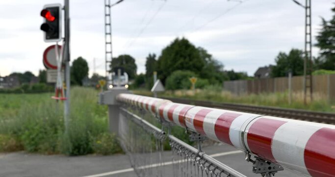 Selective focus view at red and white level crossing railway barrier which block the road and locomotive of empty freight train move on the rail on countryside in Germany.	