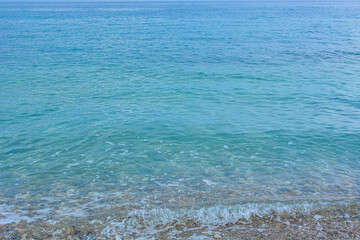 Soft wave of the turquoise sea on the tropical beach. Water surface background with copy space, pebble shore