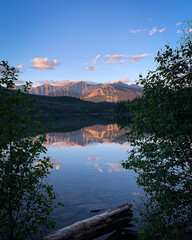 Tranquil view through trees of a mountain range and its reflection on a lake.