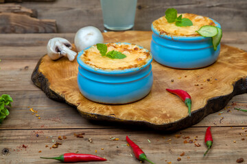 Pots with mushroom julienne on a wooden board, decorated with herbs. Julienne in cocotte with yellow cheese crust.
