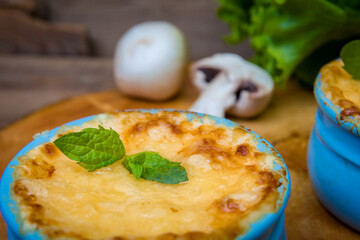 A pot of mushroom julienne on a wooden board, decorated with herbs. Julienne in cocotte with yellow cheese crust. Close-up.