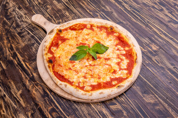 Super margherita pizza made of fine wheat flour dough with lots of cheese and lots of tomato on white plank board