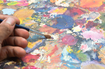 Pintura al oleo. Mano pintando en paleta de colores multicolor, verde, azul, morado, rojo....