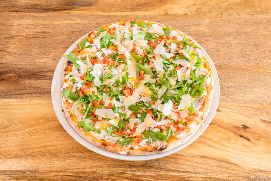 pizza with a lot of arugula and a lot of parmesan cheese in thin crust flakes and mozzarella cheese with chopped tomato