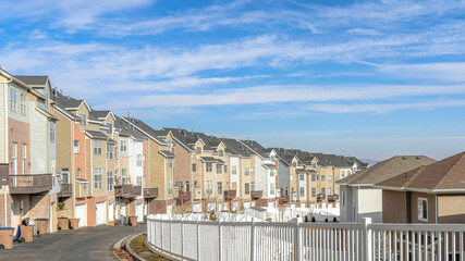Pano Townhouses along road with white fence against scenic blue sky and white clouds