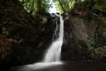 Small waterfall in Forsakar, Southern Sweden, surrounded by plants, shrubs, and bushes. Long-exposure shot.