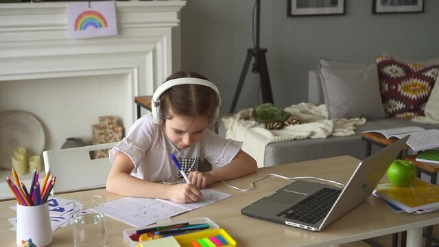 Child exercise in writing numbers with textbook Spbd. Girl in headphones sit at desk with laptop
