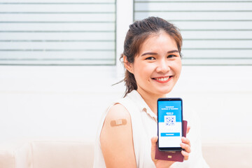 Asian young woman smile have adhesive plaster on arm her vaccinated and showing app smartphone mobile digital screen vaccinated coronavirus (COVID-19) certificate after getting vaccine prevent