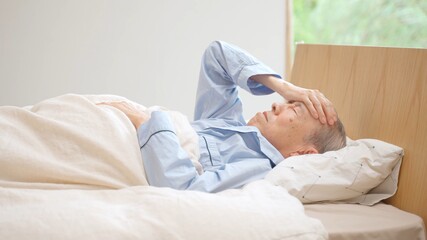 寝室で頭をおさえる高齢者