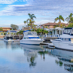 Square Yachts and boats on private docks of waterfront homes under cloudy blue sky