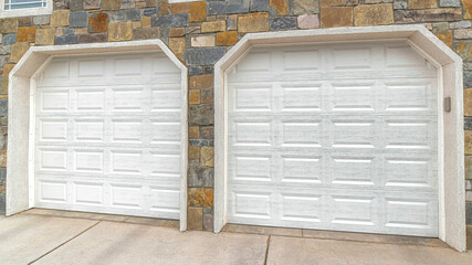 Pano Two car attached garage exterior with white doors against stone wall of a house