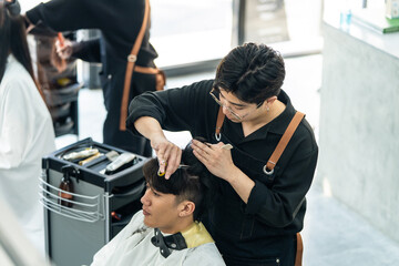 Asian hairdresser barber male cut hair of attractive man in salon shop