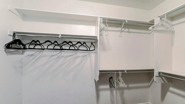 Pano Empty walk in closet of home with white wall and hanges hanging on netal rods