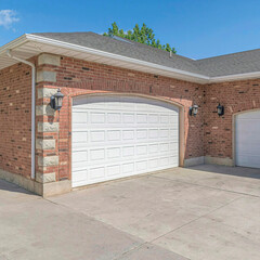 Square Building with red brick wall gray roof and two white arched wooden garage doors