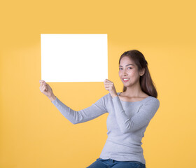 Naklejka na ściany i meble Asian woman in casual clothes holding empty blank board isolated on yellow background
