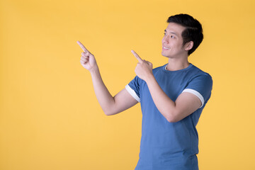 Happy Asian man pointing fingers up at empty copy space for text over yellow background