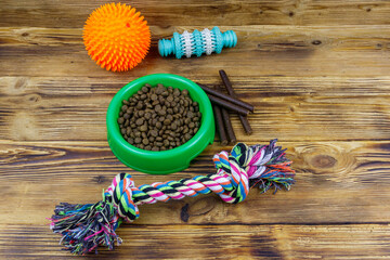Obraz na płótnie Canvas Dog toys and feed for dogs in green plastic bowl on wooden background. Dog care concept