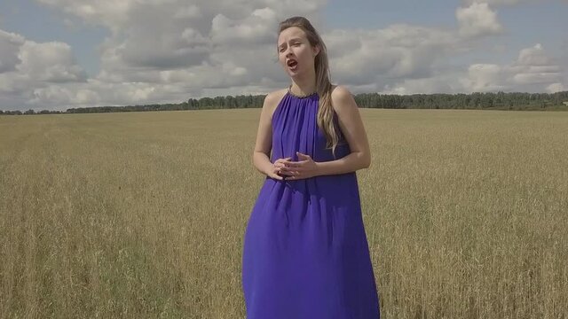 a girl in a blue dress performs a sad song in a field. Singing in nature. Shooting the clip outdoors. face close-up