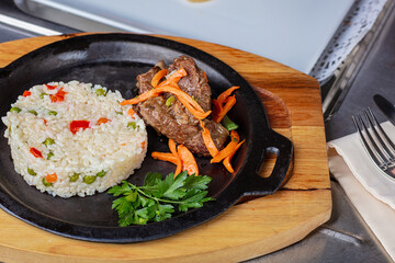 There is a hot plate with fried meat and rice with vegetables on a wooden stand.