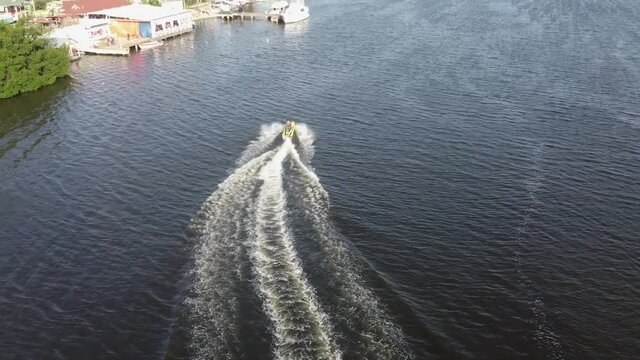 Bird's eye view Drone flight behind a jetsky traveling over the water. Sun is reflecting on the water.