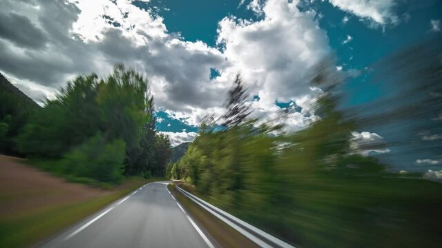 Dashcam view. Driving on the narrow country road on a sunny summer day along the forest-covered riverbank. White thick fluffy clouds hang in the blue sky.