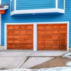 Square Exterior of home with blue wall and attached two car garage with brown doors